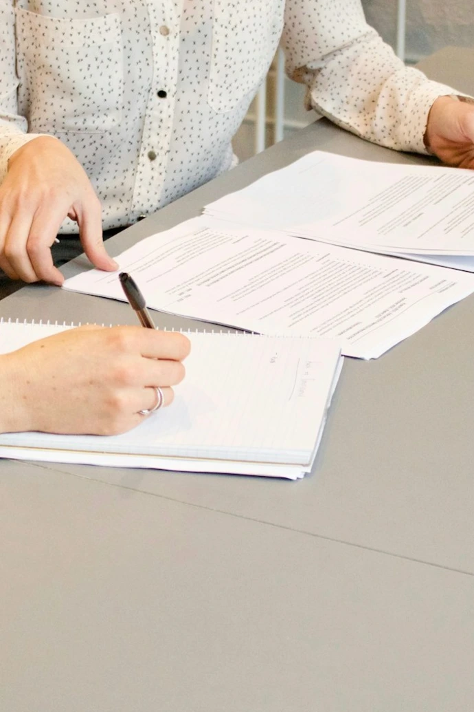 woman signing on white printer paper beside woman about to touch the documents