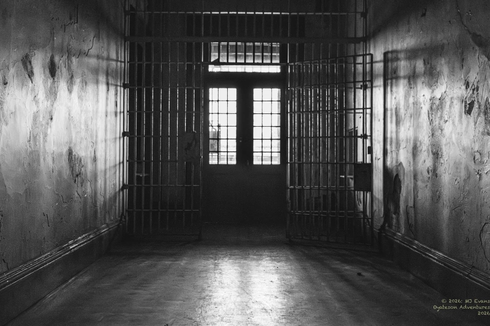 A dark, empty prison hallway with cell doors open.